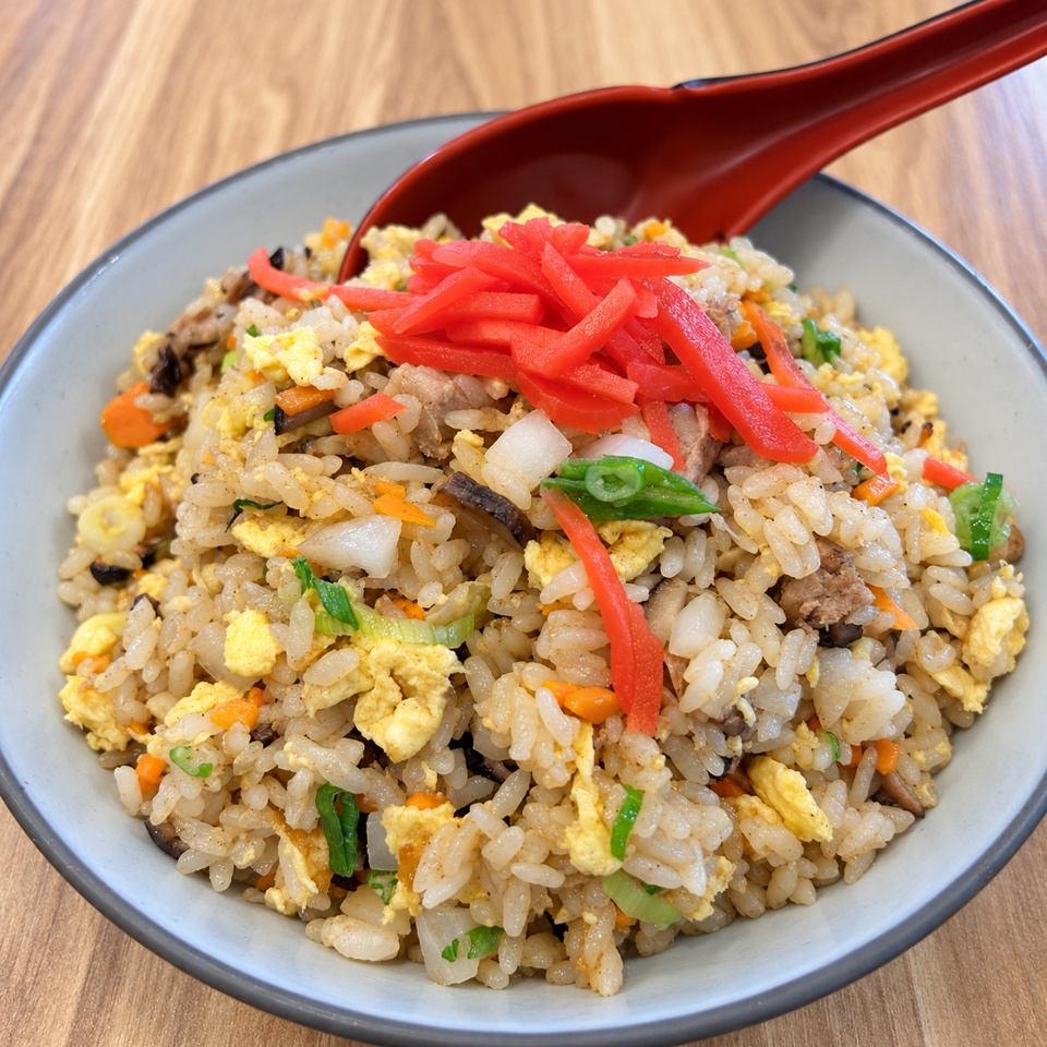 Bowl of fried rice with egg, vegetables, meat, and red pickled ginger, served with a red spoon.