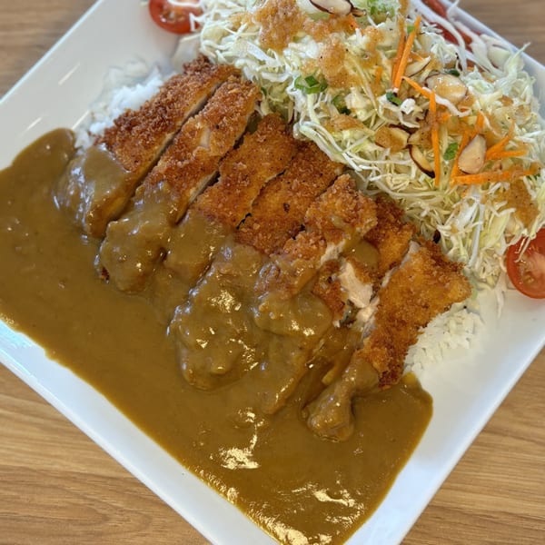 Mako Ramen's chicken katsu curry with rice and a side salad on a white rectangular plate.