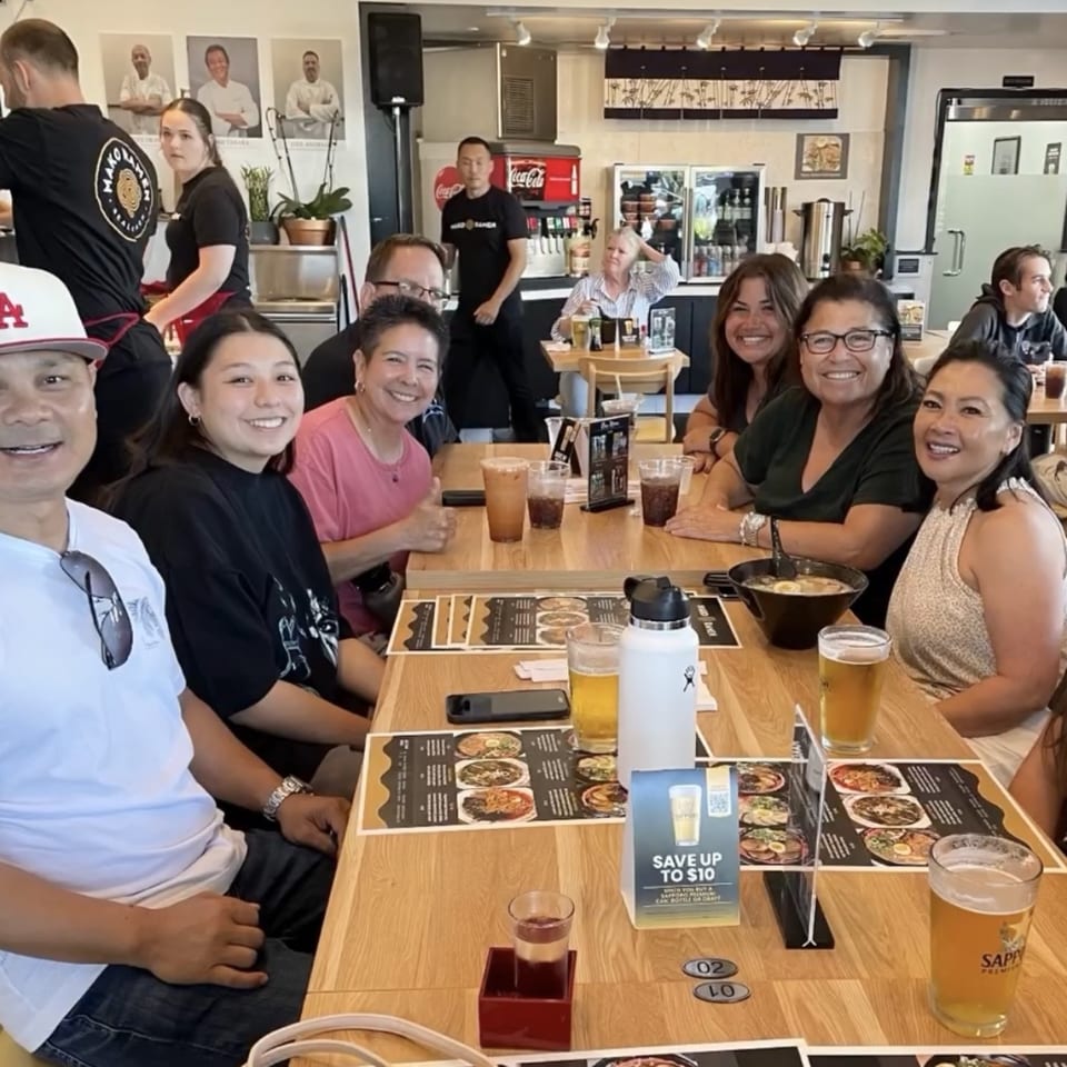 Happy customers enjoying ramen and drinks at Mako Ramen, with staff in the background.