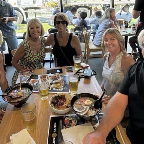 Three smiling women at a Mako Ramen table with bowls of ramen and drinks.