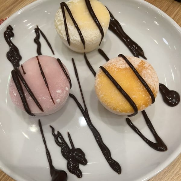 Three colorful mochi ice creams, drizzled with chocolate sauce, on a white plate.