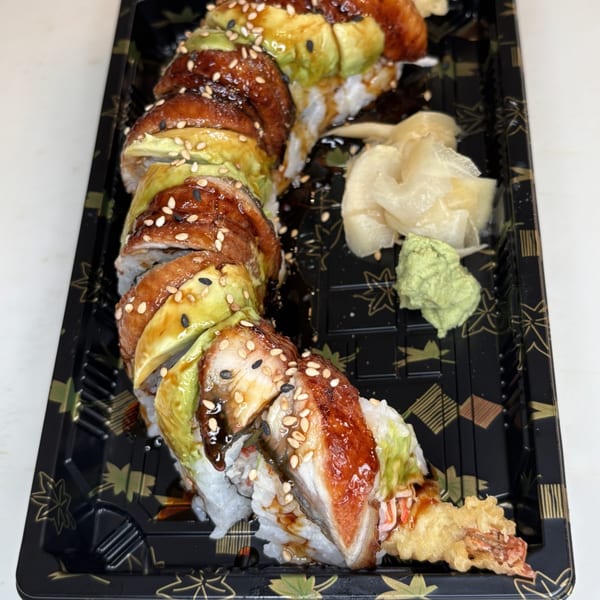 Dragon Roll sushi with eel, avocado, sesame seeds, ginger, and wasabi in a black tray.