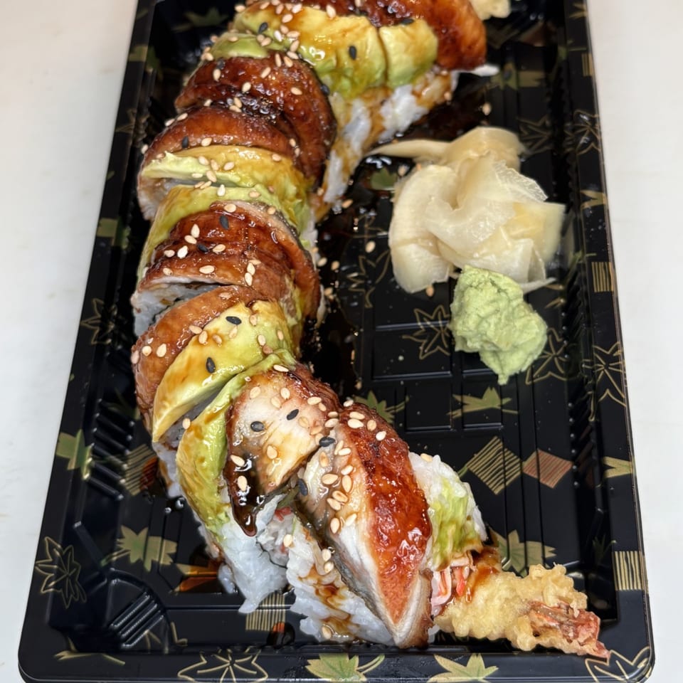 Dragon Roll sushi with eel, avocado, sesame seeds, ginger, and wasabi in a black tray.