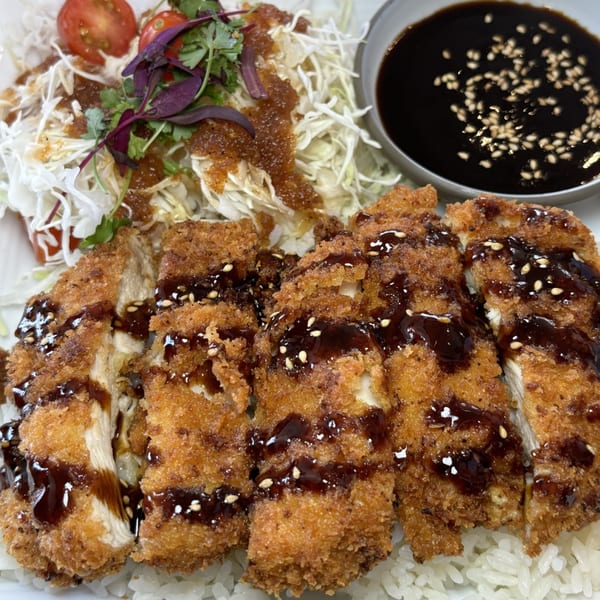 Crispy chicken katsu drizzled with sauce, served with shredded cabbage, cherry tomatoes, and rice.