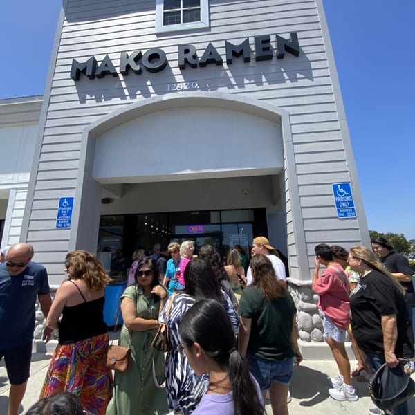 A crowd of people waiting in line outside Mako Ramen restaurant on a sunny day.