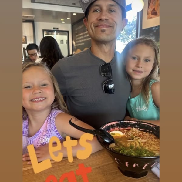 A man and two young girls smiling with a bowl of Mako Ramen in the foreground.