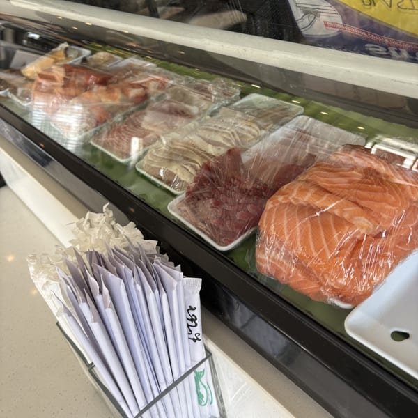 Raw fish, including salmon, tuna, and other cuts, wrapped in plastic in a display case at Mako Ramen.