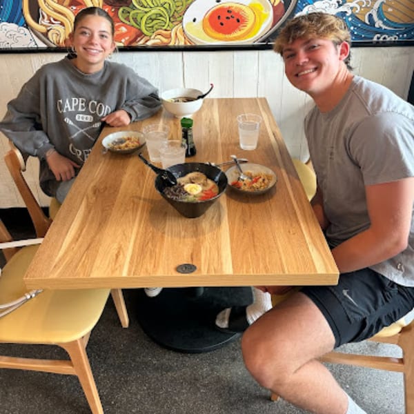 Two happy customers enjoying ramen bowls at a wooden table in Mako Ramen.
