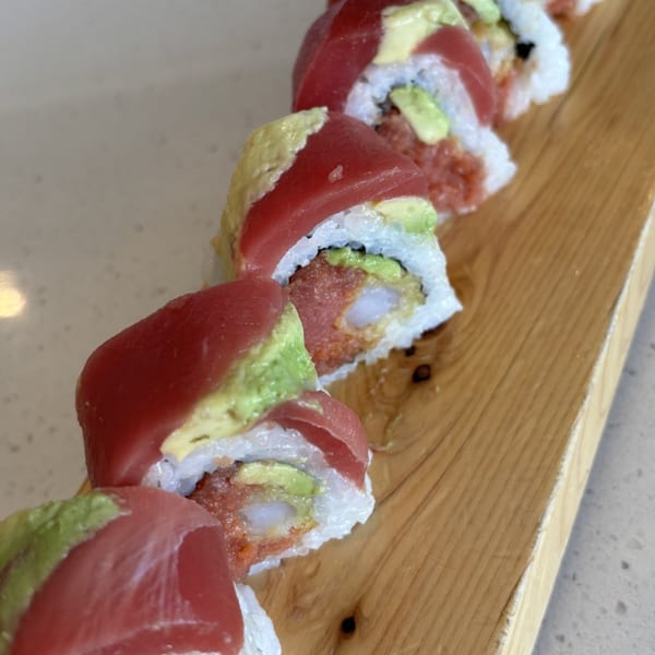 A row of Mako Ramen sushi rolls with tuna, avocado, and shrimp on a wooden board.