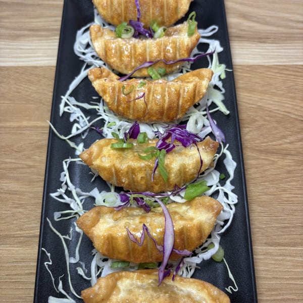 Golden-brown gyoza dumplings, garnished with shredded cabbage, green onions, and purple cabbage, on a black plate.