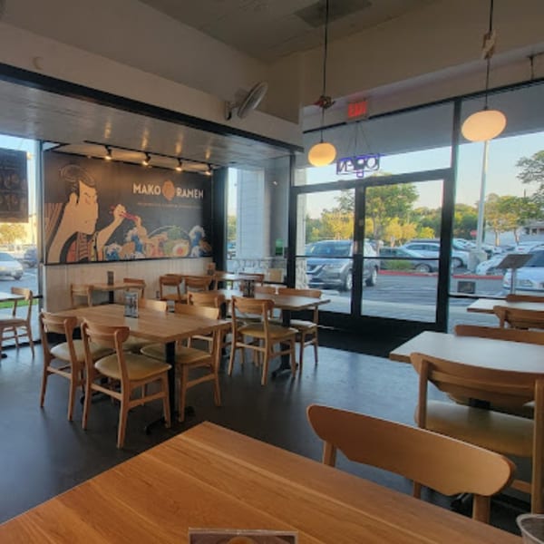 Interior of Mako Ramen with light wooden tables and chairs, and a large mural of a person eating ramen.