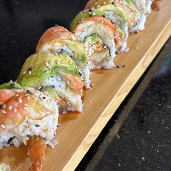 Shrimp tempura and avocado sushi rolls with sesame seeds on a wooden board.