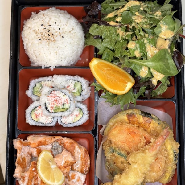 A bento box with white rice, salad, California rolls, grilled salmon, and tempura shrimp and vegetables.