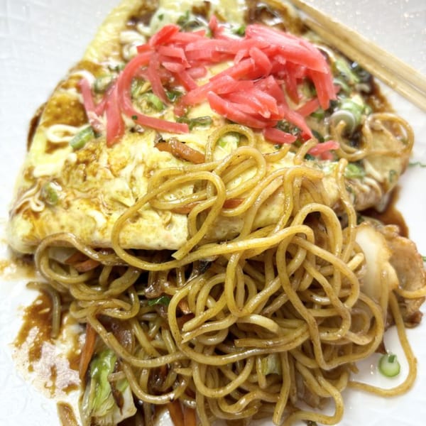 Omelet-covered yakisoba noodles topped with red pickled ginger, green onions, and sauce.