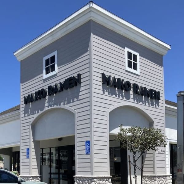 Exterior of Mako Ramen restaurant with light gray siding, black signage, and a small tree.