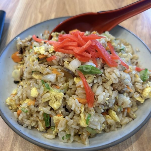 A close-up of Mako Ramen's fried rice, topped with red pickled ginger and a red spoon.