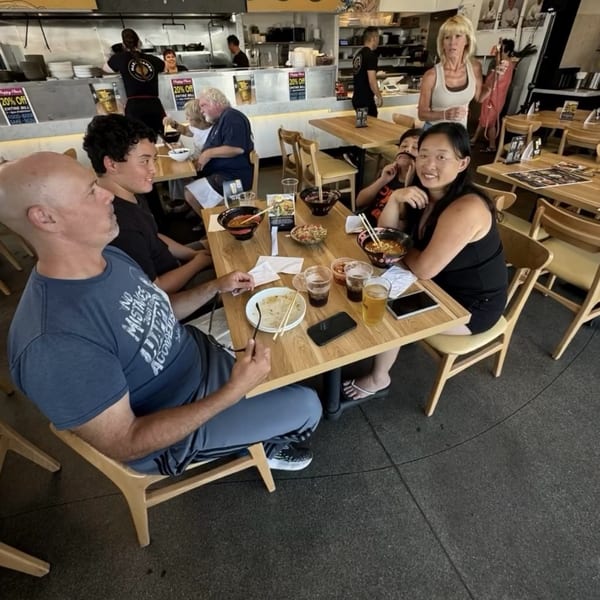 Customers enjoying ramen and drinks at wooden tables in a brightly lit Mako Ramen restaurant.