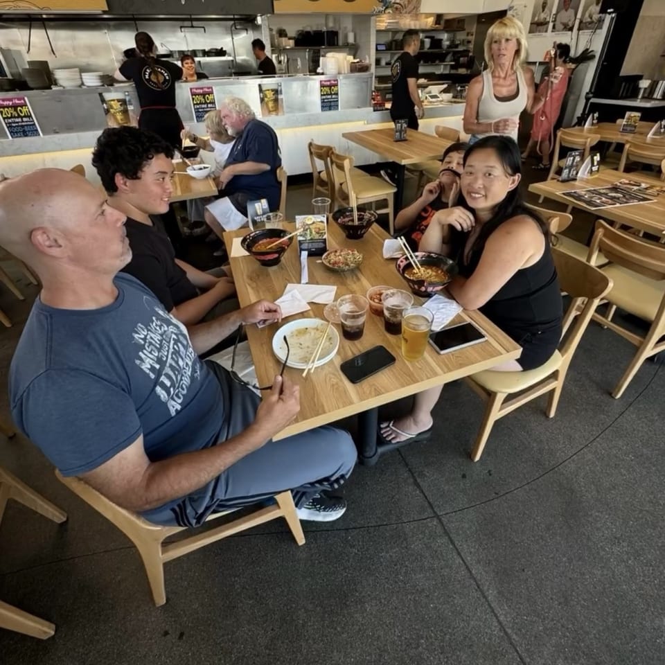 Customers enjoying ramen and drinks at wooden tables in a brightly lit Mako Ramen restaurant.