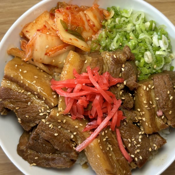 A close-up of a Mako Ramen bowl with braised pork belly, kimchi, green onions, and pickled ginger.